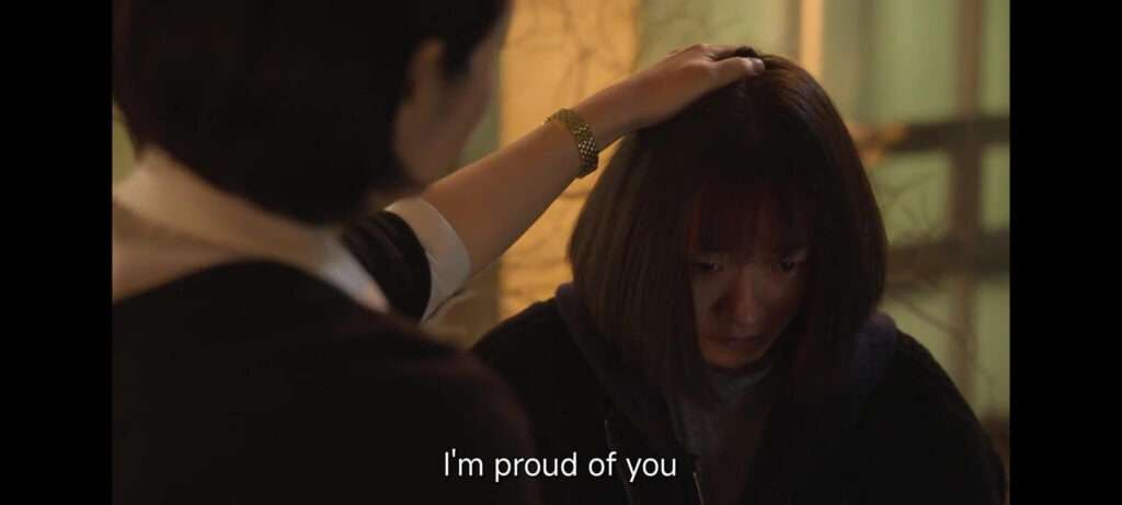 Juíza Shim passando a mão na cabeça de uma jovem com a legenda de sua fala, dizendo "estou orgulhosa de você"