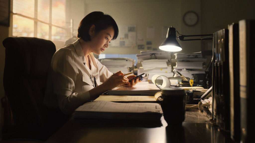 Juíza Shim Eun Seok em sua mesa de escritório com o celular em uma mão e um lápis na outra