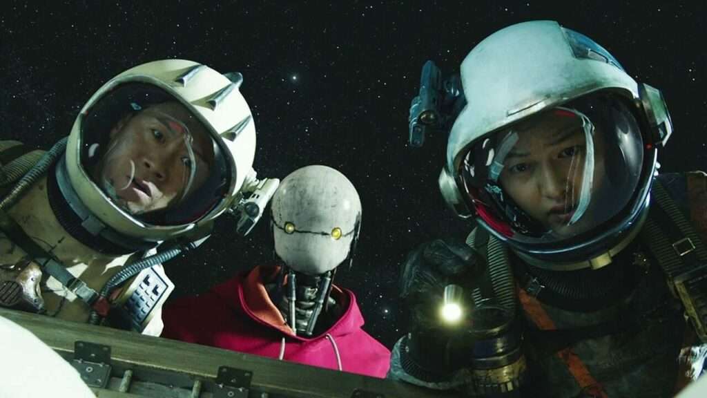 Tiger, Bubs e Kim Tae Ho em roupa de astronauta olhando para a tela